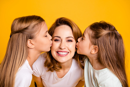 Close-up portrait of three nice cute adorable winsome lovely sweet tender attractive cheerful cheery positive people kissing mum having fun feelings isolated over bright vivid shine yellow background