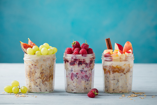 Overnight oats, bircher muesli with fresh berries and fruits in a glass jars on wooden table background. Copy space