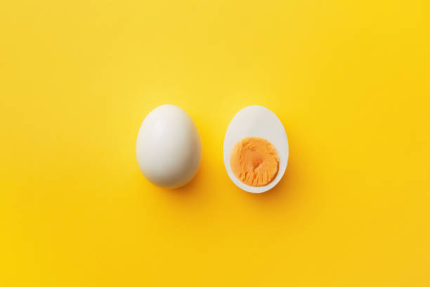 Single whole white egg and halved boiled egg with yolk on a yellow background. Top view stock photo