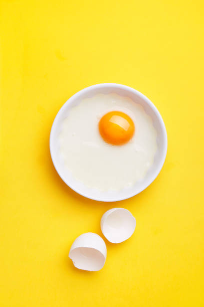 White egg yolk in a bowl on a yellow background. Egg shell on the side. Top view. Copy space