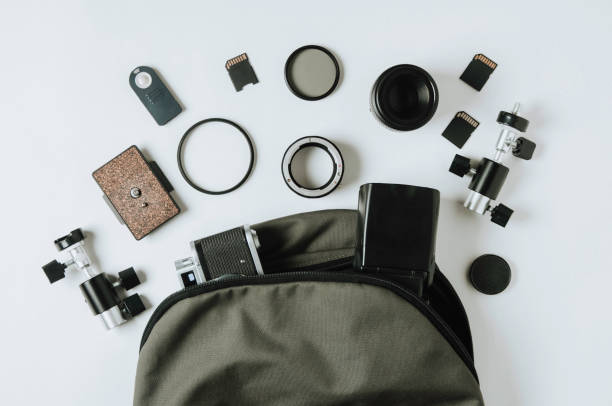 Old camera, green backpack and photo accessories on pale background