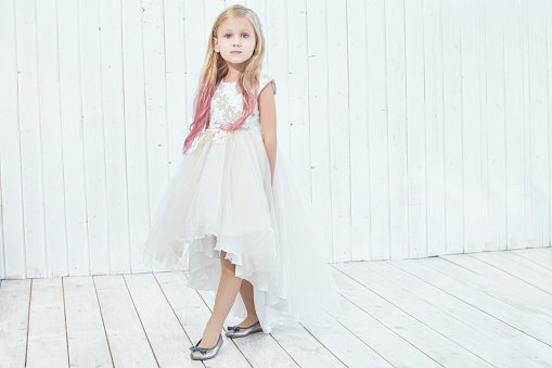 Pensive, dreamy. One little cute Caucasian girl in white summer clothes sitting on big box looking away isolated over white studio background. Copyspace for advertisement