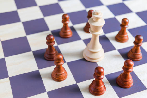 istock Black chess pawns surround the white king in a group on the chessboard 1128033280