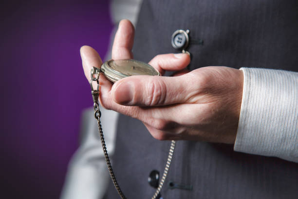 man in elegant suit on purple background reading the time in his pocket watch stock photo