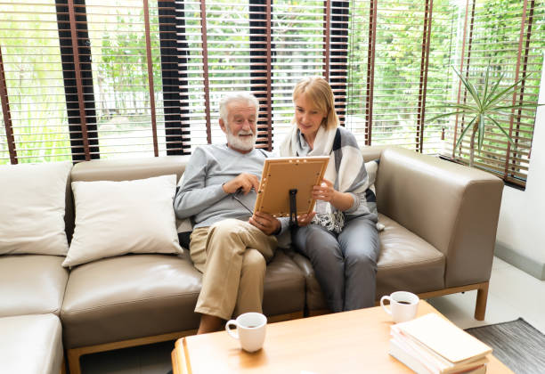 istock Two elderly people enjoying spending time together while sitting on sofa and looking at old photographs in picture frame at home, 1128040446