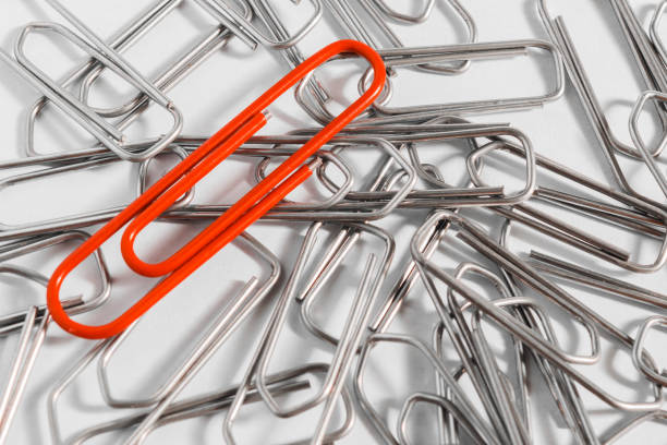 A red paper clip in a group of metal staples A red paper clip in a group of metal staples documento stock pictures, royalty-free photos & images