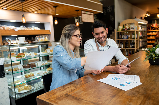 Female business owner of a cafeteria going over some documents with male manager both smiling very happy