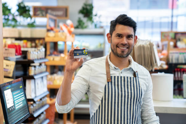 istock Handsome sales clerk holding a loyalty program card while facing camera smiling at the supermarket 1128048553