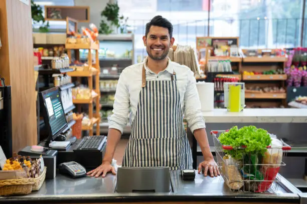 Handsome cashier at a supermarket facing camera smiling at the supermarket **DESIGN ON SCREEN WAS MADE FROM SCRATCH BY US**