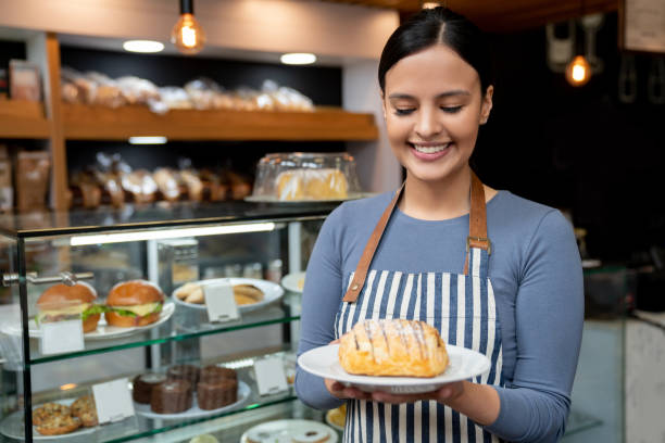 istock Cheerful waitress at a cafeteria holding a delicious chocolate bread looking at it smiling 1128048601