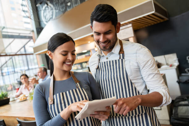 istock Latin american friendly manager and waitress looking at something on notepad smiling 1128048616