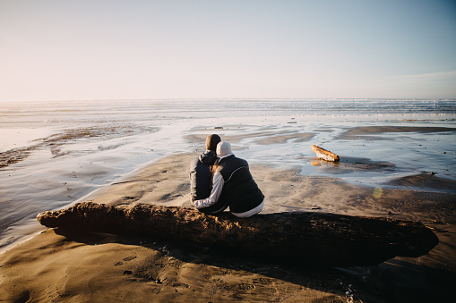 A senior couple explores a beach in Oregon state, enjoying the beauty of sunset on the Pacific Northwest coast.  The hug, enjoying being together and watching the ocean view.