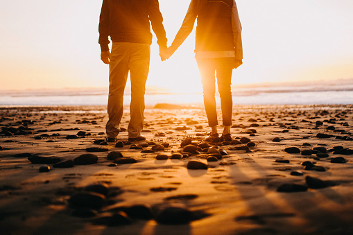 A senior couple explores a beach in Oregon state, enjoying the beauty of sunset on the Pacific Northwest coast.  They stand hand in hand, watching the ocean view.