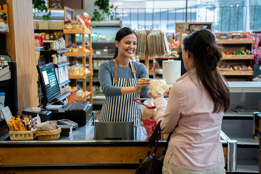 Unrecognizable customer at supermarket handing products to friendly cashier smiling for checkout **DESIGN ON SCREEN WAS MADE FROM SCRATCH BY US**