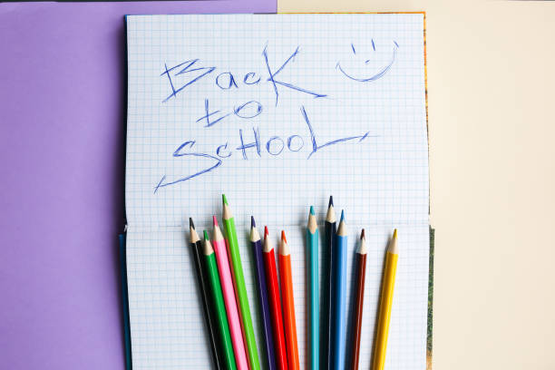 istock Color pencils lying on pastel purple and beige background. Squared notebook with back to school concept sign and smile. Colorful art studying and painting. Copy space place for postcard wish. 1128054237
