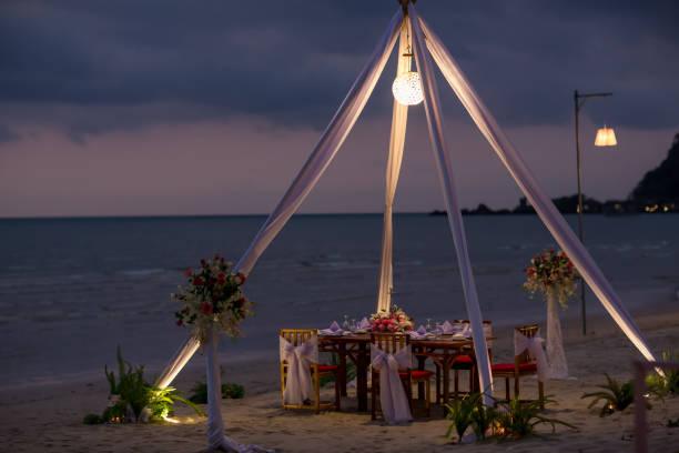 istock Romantic dinning table on the beach . Table setting at a luxury wedding and Beautiful flowers on the table. 1128054399