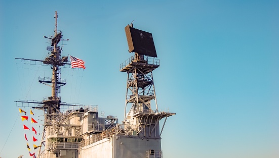 The mast of this naval ship stands high, reading to the sky.  This mast is an important element of the ship for communication and identification.