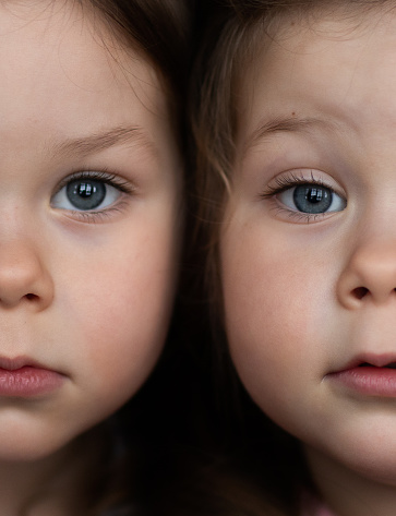 A portrait of identical twin toddler girls next to each other with different facial expressions