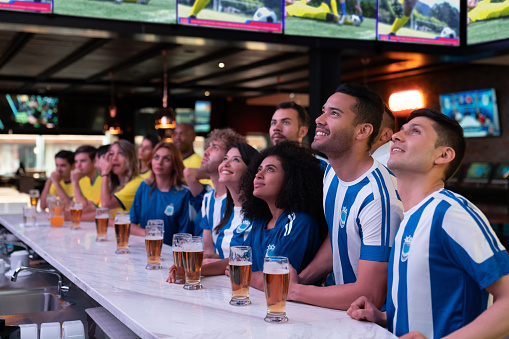 Happy group of football fans watching the game at a sports bar and drinking a beer