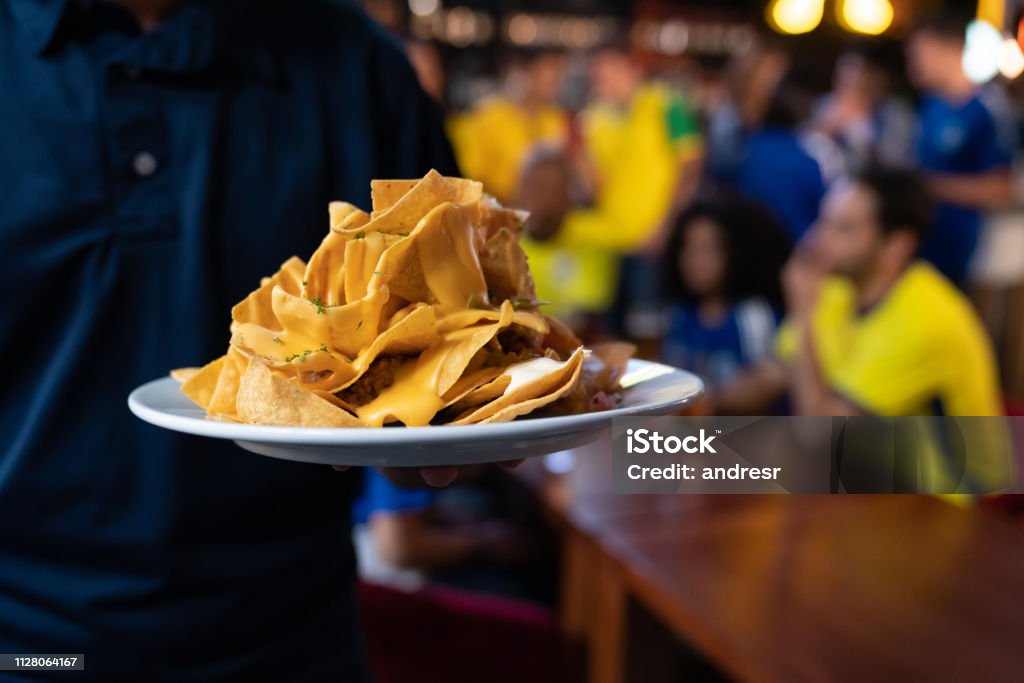 Close-up on a waiter serving nachos at a sports bar Close-up on a waiter serving nachos at a sports bar - lifestyle concepts Bar - Drink Establishment Stock Photo
