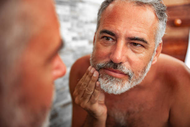 istock Sunburned Mature Man looking into the Mirror in the bathroom 1128066192