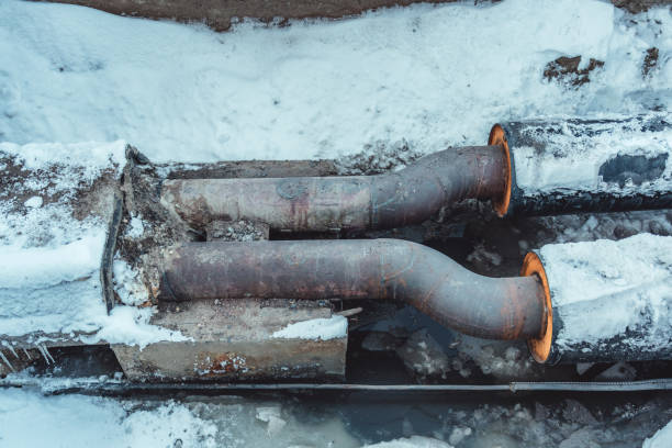 Two welded steel pipes with insulation in a snowy trench with some water in the bottom