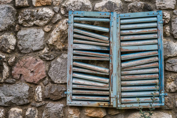 Closed damaged blue wooden window shutter on the wall of an old building