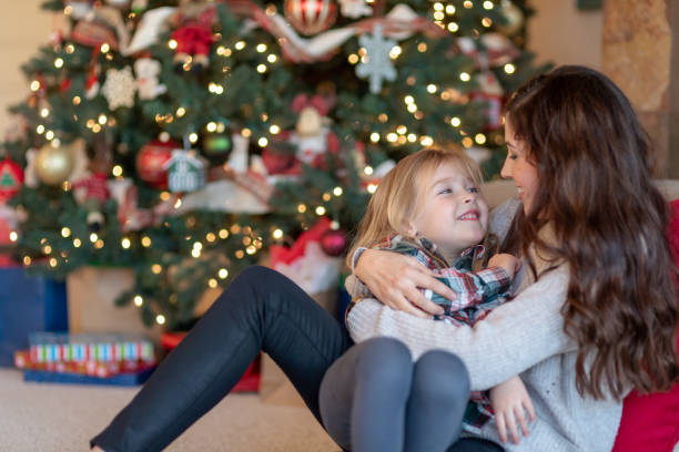 istock Mom snuggles with her daughter by the Christmas tree 1128073535
