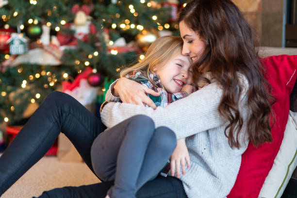 istock Mom snuggles with her daughter by the Christmas tree 1128073573
