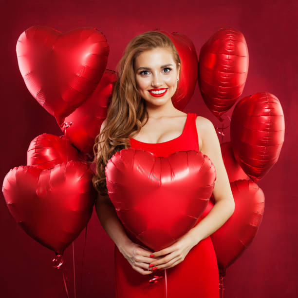 Beautiful woman in red dress and red heart balloons on holiday party celebration background Beautiful woman in red dress and red heart balloons on holiday party celebration background valentine s day holiday stock pictures, royalty-free photos & images