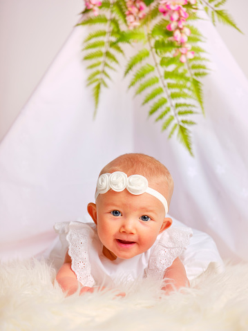 A happy six month old baby girl in a white studio setting.