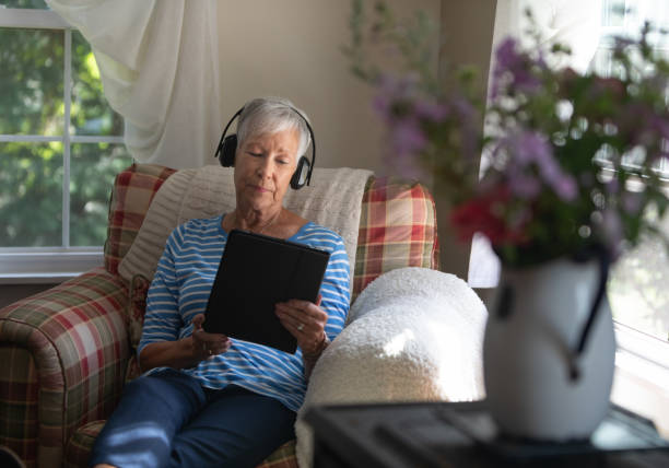 atrakcyjna starsza kobieta za pomocą cyfrowego tabletu noszącego słuchawki bezprzewodowe - ipad senior adult 70s adult zdjęcia i obrazy z banku zdjęć