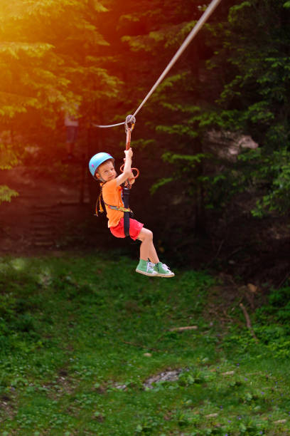 Happy kid with helmet and harness on zip line between trees