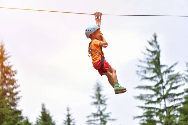 Happy kid with helmet and harness on zip line between trees stock photo