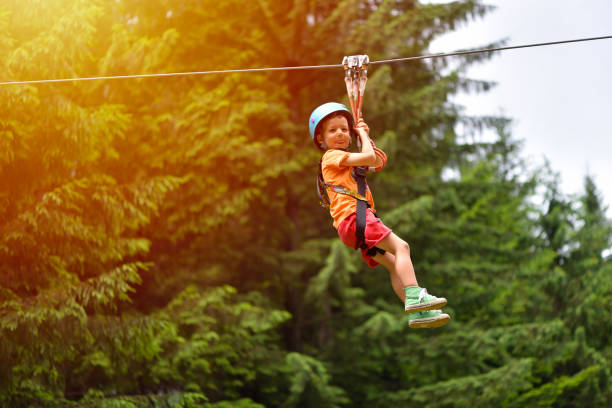 Happy kid with helmet and harness on zip line between trees stock photo