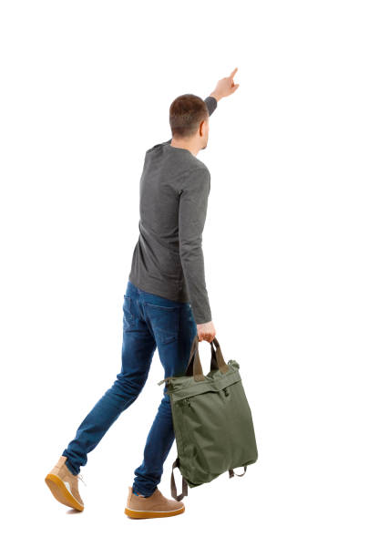istock Back view of a walking man with a bag pointing his hand up. 1128101545