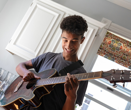 Smiling teenage mixed race boy playing guitar in the kitchen