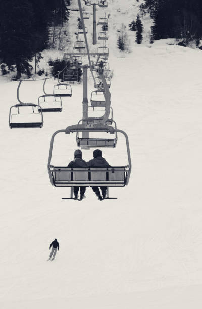 Two skiers on chair-lift in gray winter day Two skiers on chair-lift in gray winter day. Caucasus Mountains. Hatsvali, Svaneti region of Georgia. Black and white toned landscape. skiing photos stock pictures, royalty-free photos & images