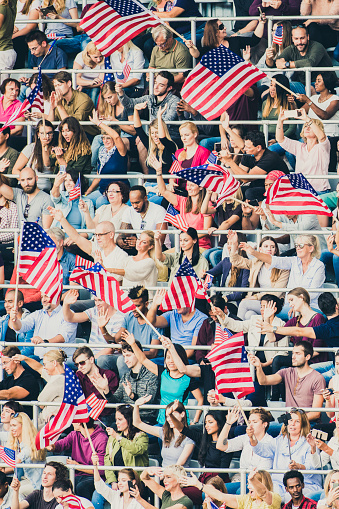 Vertical photo of a crowd of US sports fans waving American flags on a stadium during championship.