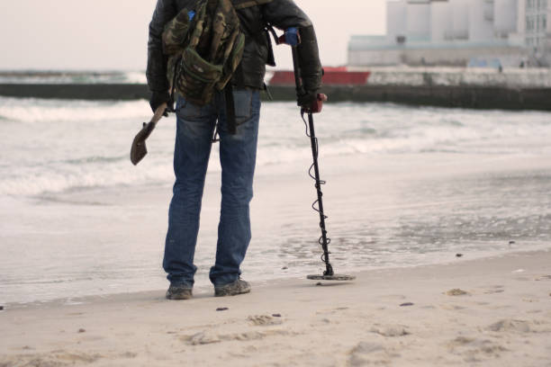 istock Black digger. Man with metal detector on the beach looking for lost objects under the sand of the ocean, sea 1128115592