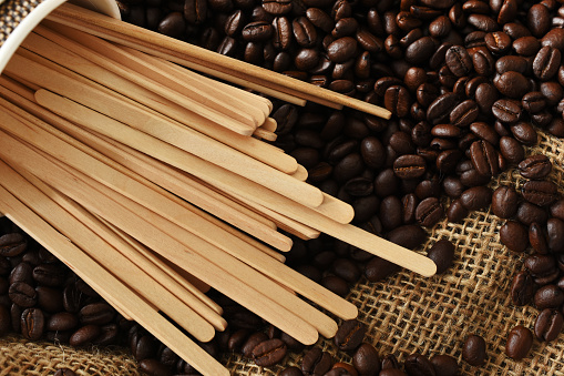 A top view image of wooden stir sticks and coffee beans.