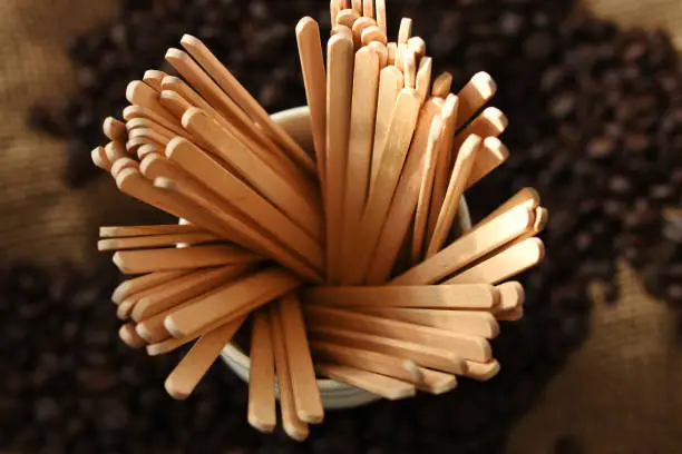 A top view image of wooden stir sticks and coffee beans.