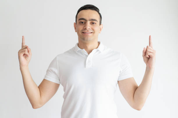 istock Smiling young guy pointing upwards and looking at camera 1128133809