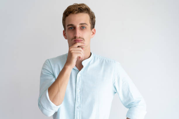 istock Pensive young man touching chin and looking at camera 1128134631