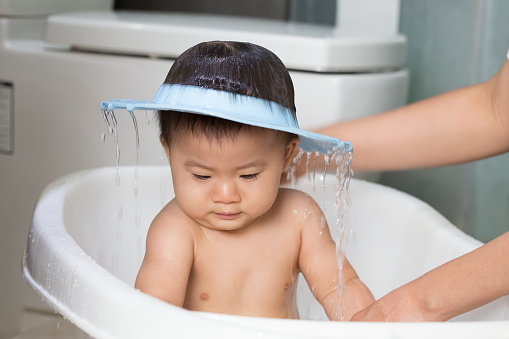 Asian baby boy taking a bath by mom and wearing shower cap. Hygiene and care for young children concept