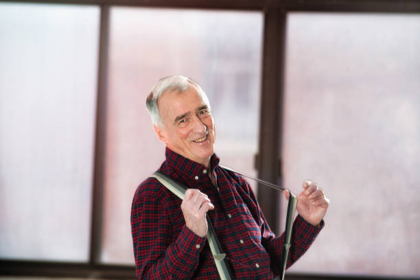lächelnder senior mann in seinen späten 70er jahren spielerisch zieht seine hosenträger - canadian culture flash stock-fotos und bilder