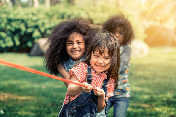 happy children playing tug of war and having fun during summer camping in the park. children recreation concept. - tug o war imagens e fotografias de stock