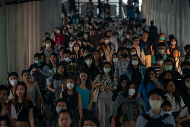 Group of many salary man wearing face mask for protect micro dust in air while going to their workplace during pm2.5 air pollution crisis in Bangkok at moring rush hour. Group of many salary man wearing face mask for protect micro dust in air while going to their workplace during pm2.5 air pollution crisis in Bangkok at moring rush hour. bts skytrain stock pictures, royalty-free photos & images