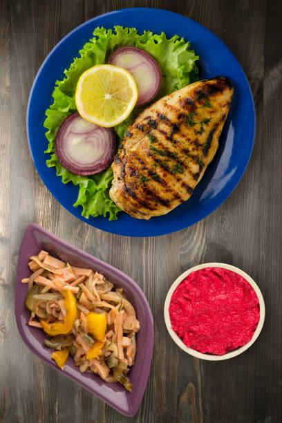 grilled chicken fillet with vegetables (lemon, salad, onion) on a wooden background. chicken fillet grilled on a plate