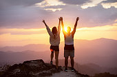 Happy couple raised arms sunset mountain top